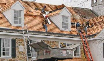 4 people using ladders to climb up on roof to install wood roofing