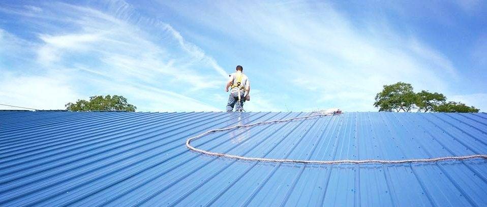 Man with safety harness walking on blue metal roofing