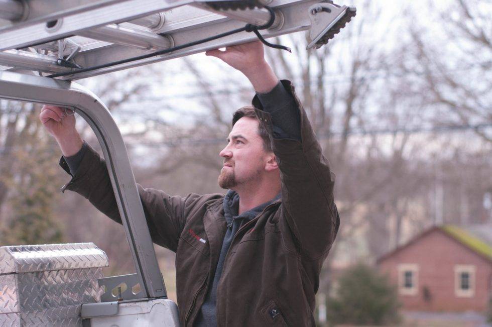 man grabbing ladder on top of truck