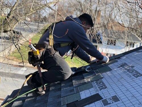 Roofer installing roofing while wearing a harness