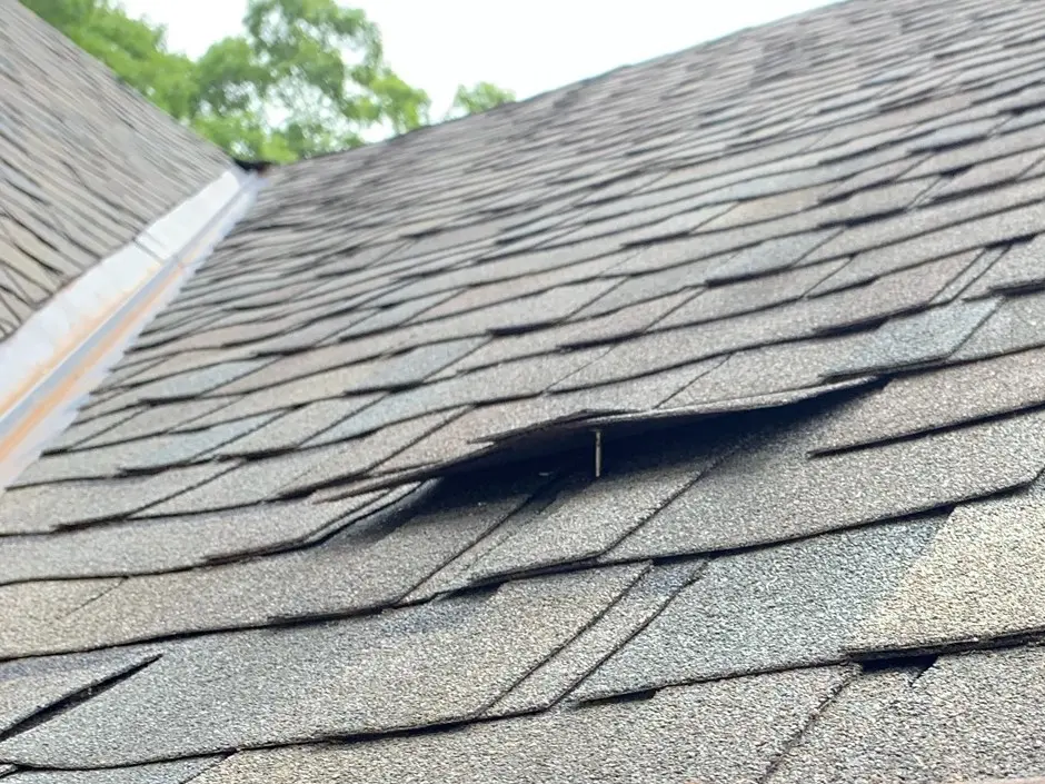 Picture of a damaged roof showing many of the shingles being lifted off due to nail pops